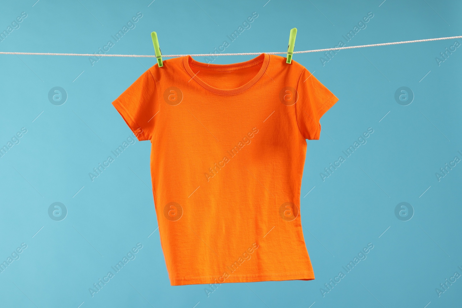 Photo of One orange t-shirt drying on washing line against light blue background
