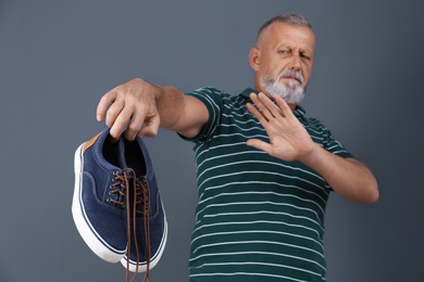 Photo of Man feeling bad smell from shoes on color background. Air freshener