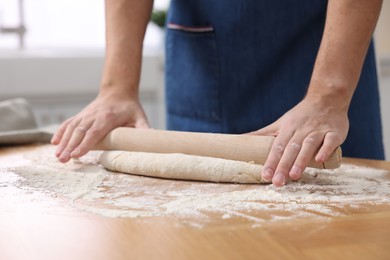 Photo of Making bread. Man rolling dough at wooden table in kitchen, closeup
