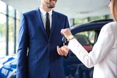 Photo of Salesperson giving car keys to man in auto dealership, closeup