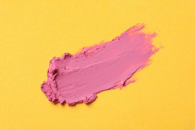 Photo of Smear of bright lipstick on yellow background, top view