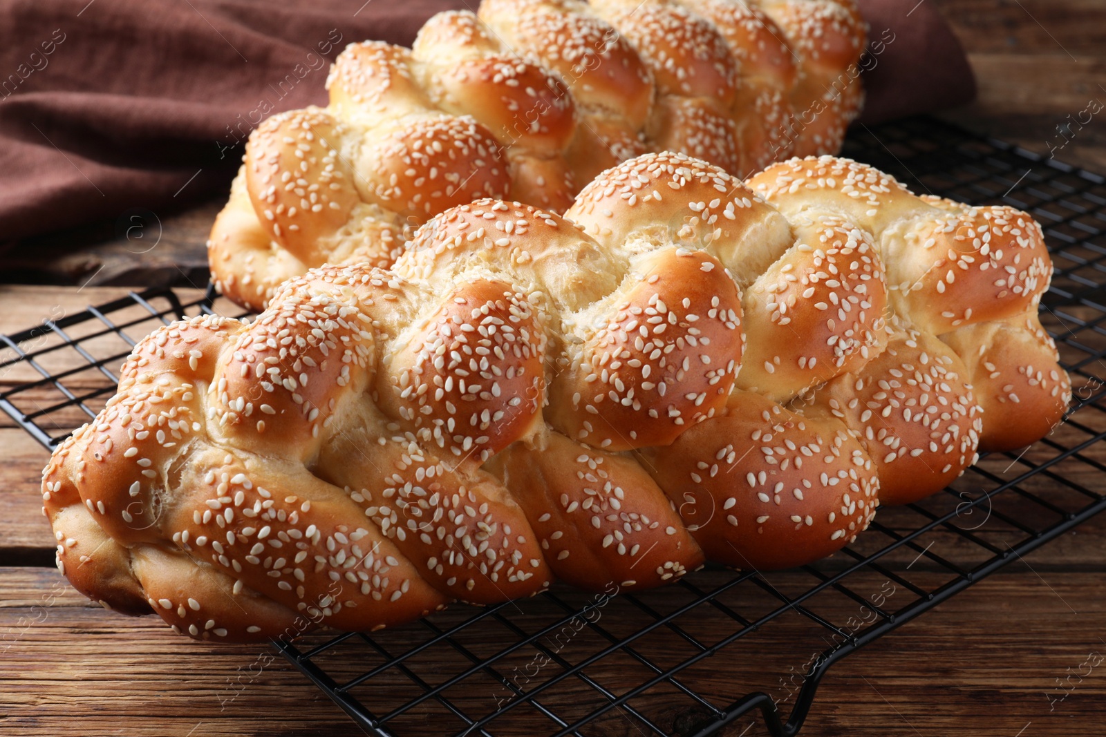 Photo of Homemade braided breads with sesame seeds on wooden table, closeup. Challah for Shabbat