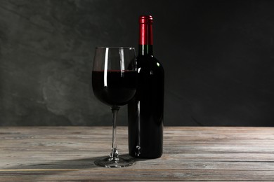Glass and bottle of red wine on wooden table against grey background