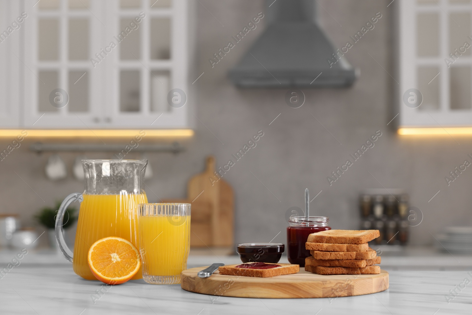 Photo of Breakfast served in kitchen. Crunchy toasts, jam and orange fresh on white table