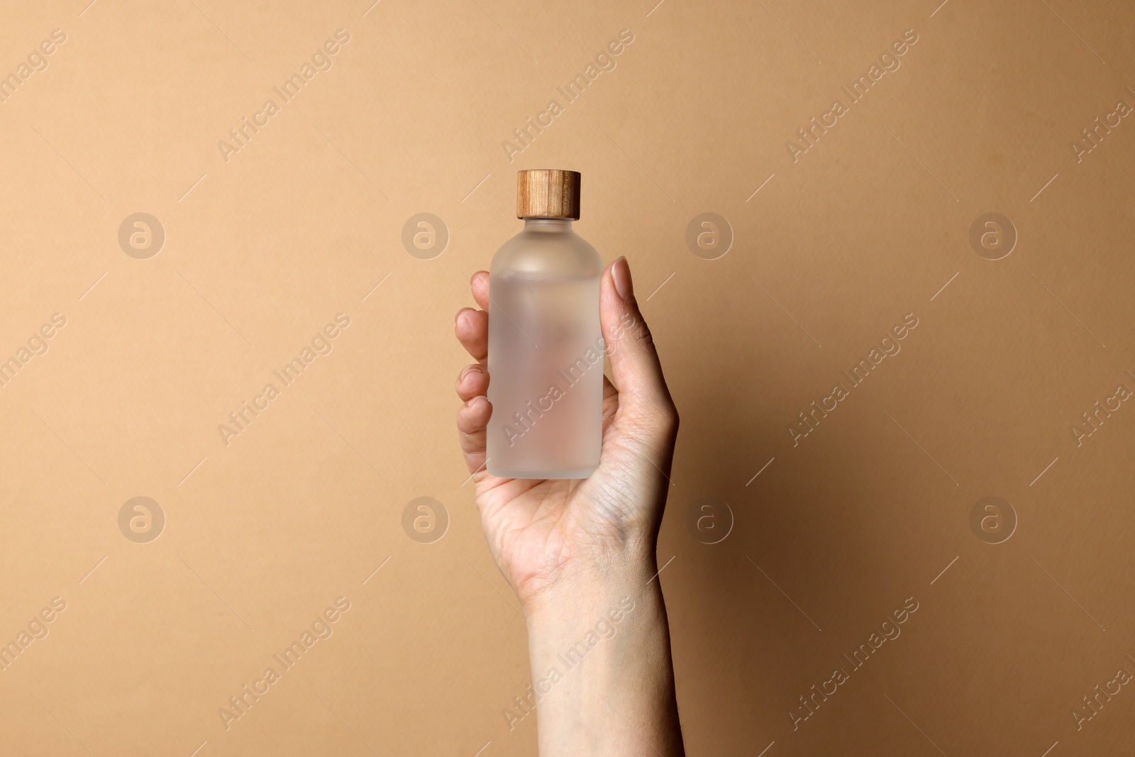 Photo of Woman holding bottle of cosmetic product on beige background, closeup
