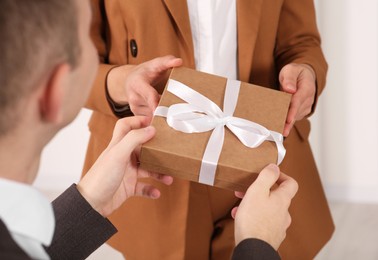 Photo of Woman presenting gift box to his colleague indoors, closeup