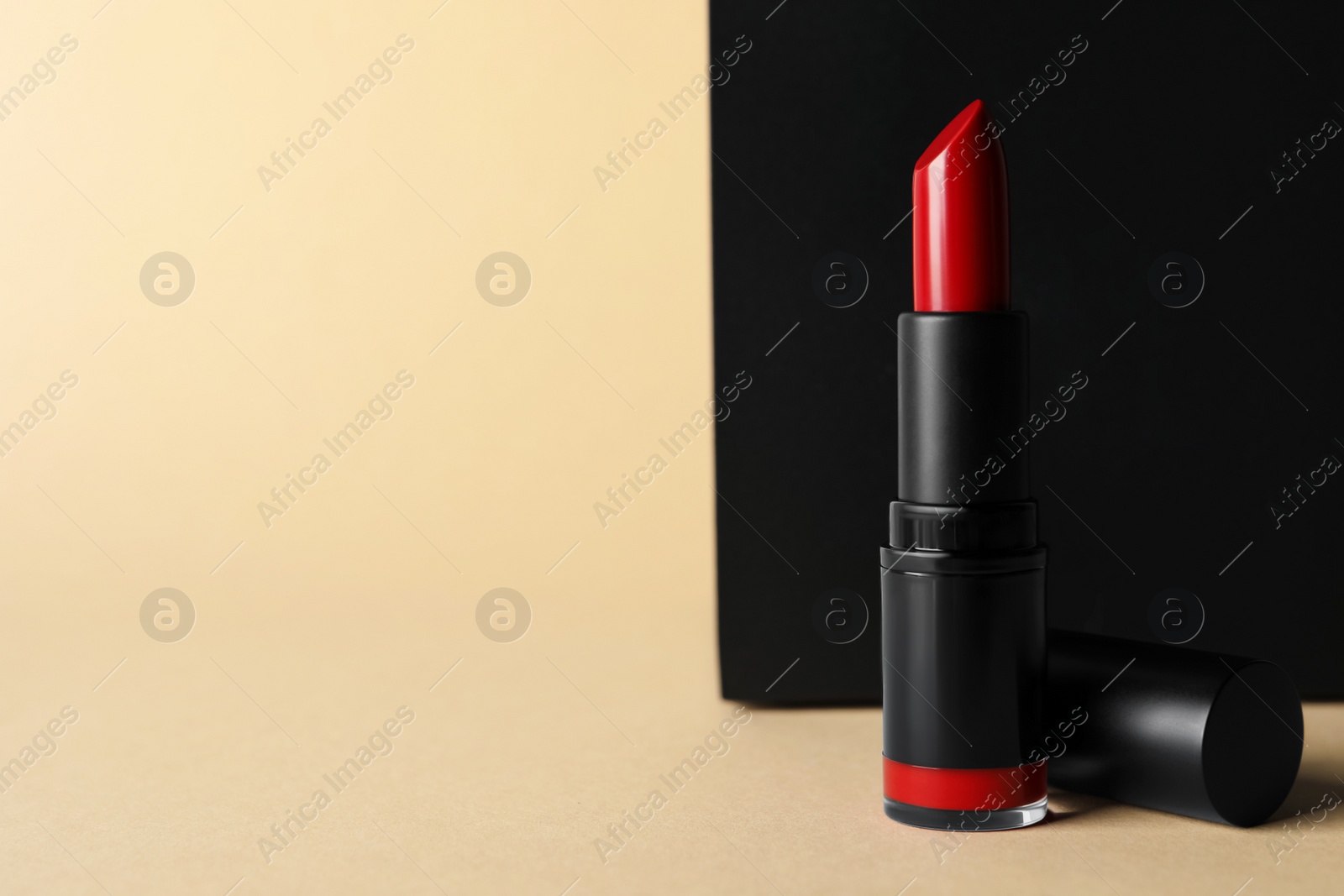 Photo of Beautiful glossy red lipstick on beige background, space for text