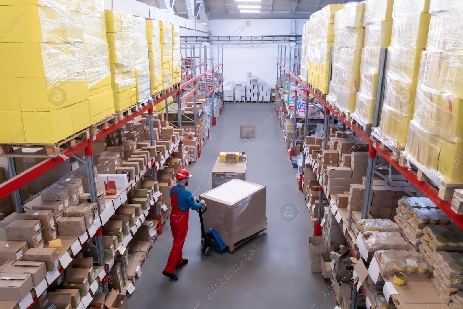 Image of Man in hardhat working with pallet truck at warehouse. Logistics center