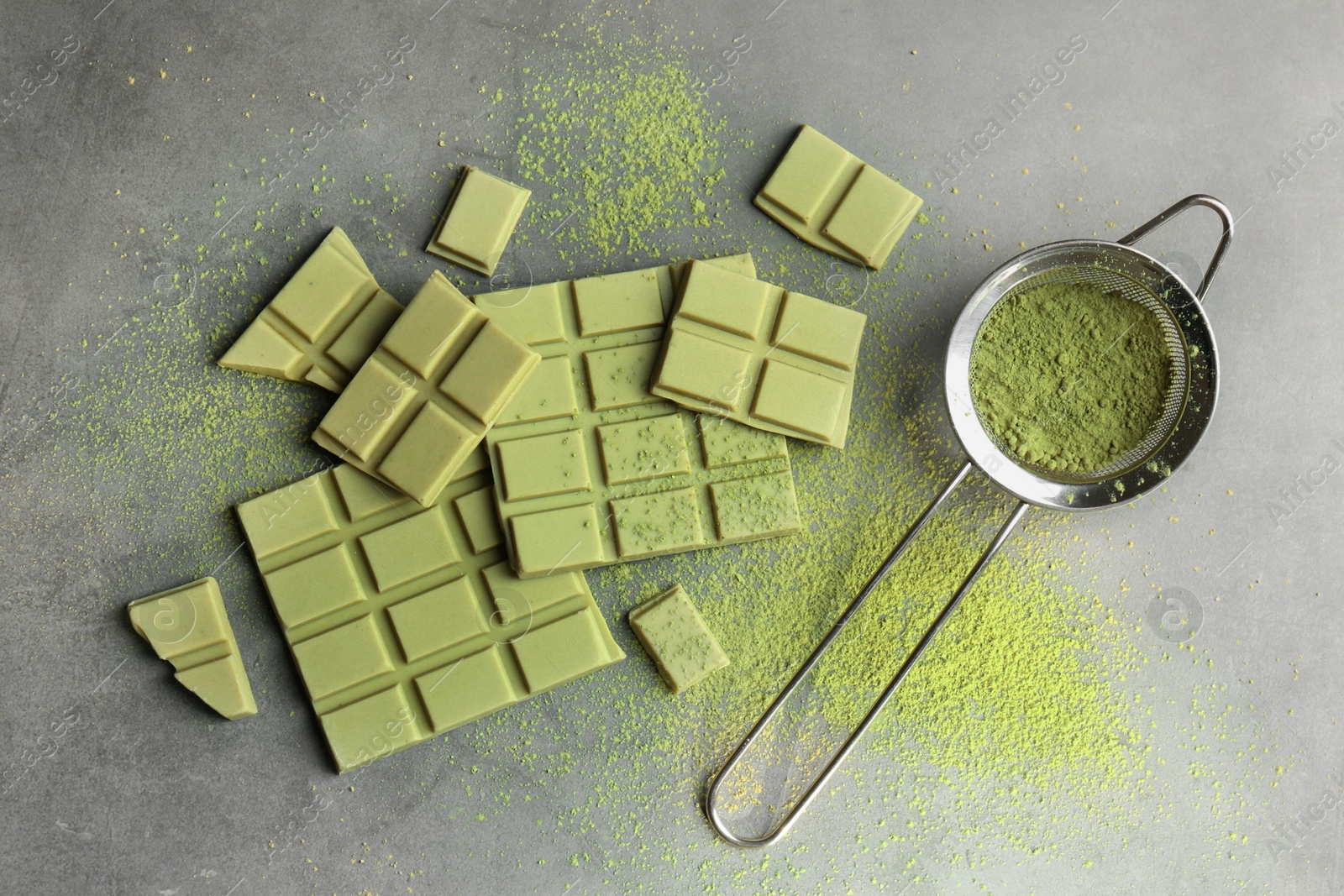 Photo of Pieces of tasty matcha chocolate bars and powder on grey textured table, flat lay
