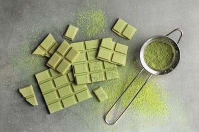 Pieces of tasty matcha chocolate bars and powder on grey textured table, flat lay