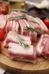 Photo of Cut raw pork ribs with rosemary on wooden board, closeup