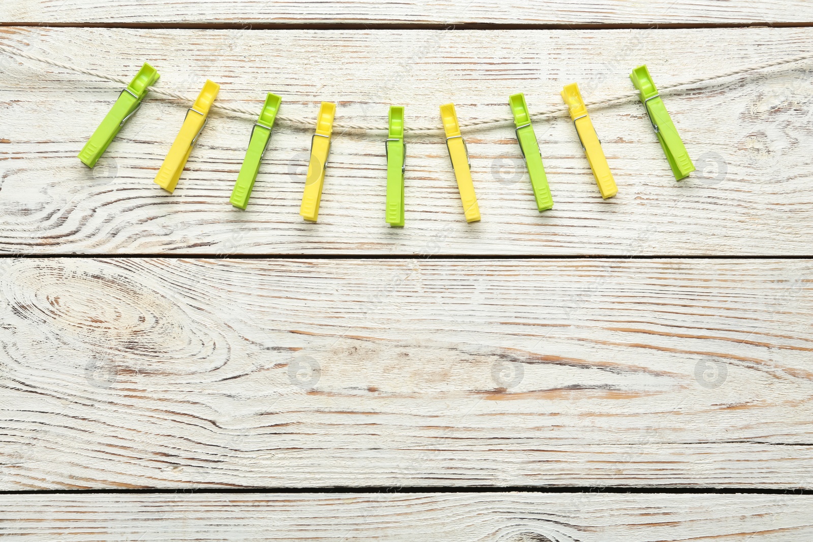 Photo of Colorful plastic clothespins and rope on white wooden background. Space for text