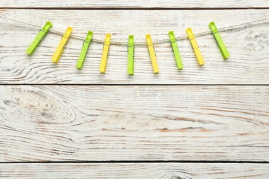 Colorful plastic clothespins and rope on white wooden background. Space for text