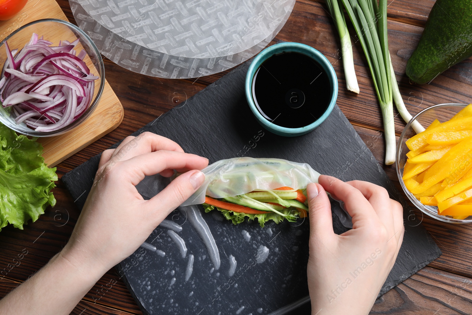 Photo of Woman wrapping spring roll at wooden table with products, top view