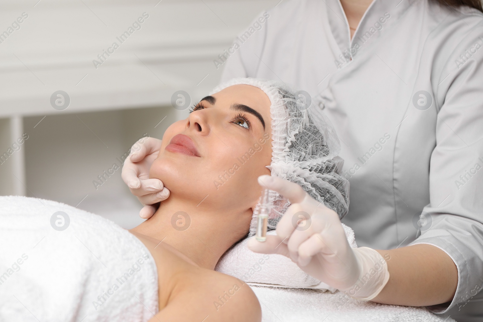 Photo of Professional cosmetologist holding skincare ampoule while working with client in clinic, closeup