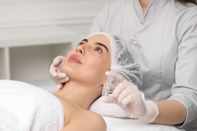 Professional cosmetologist holding skincare ampoule while working with client in clinic, closeup