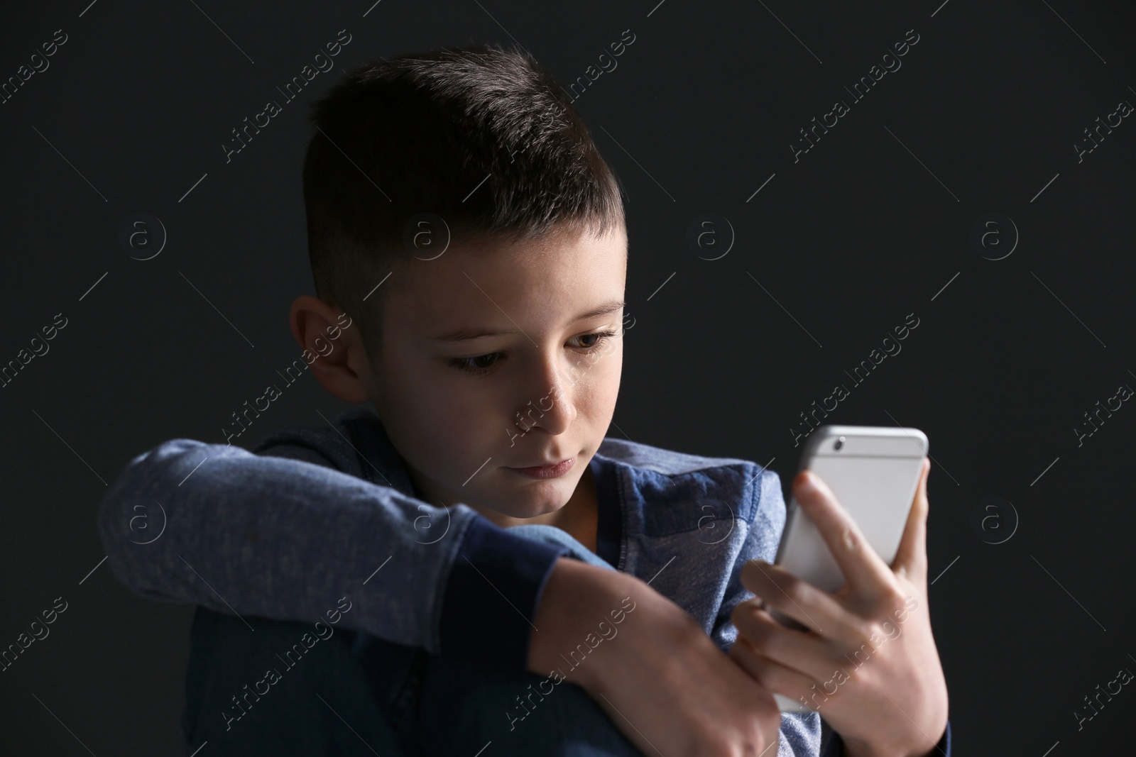 Photo of Upset boy with smartphone on dark background. Space for text