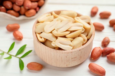 Photo of Fresh peanuts in bowl and twig on white table, closeup