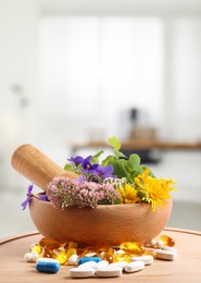 Mortar, fresh herbs and pills on wooden board in medical office