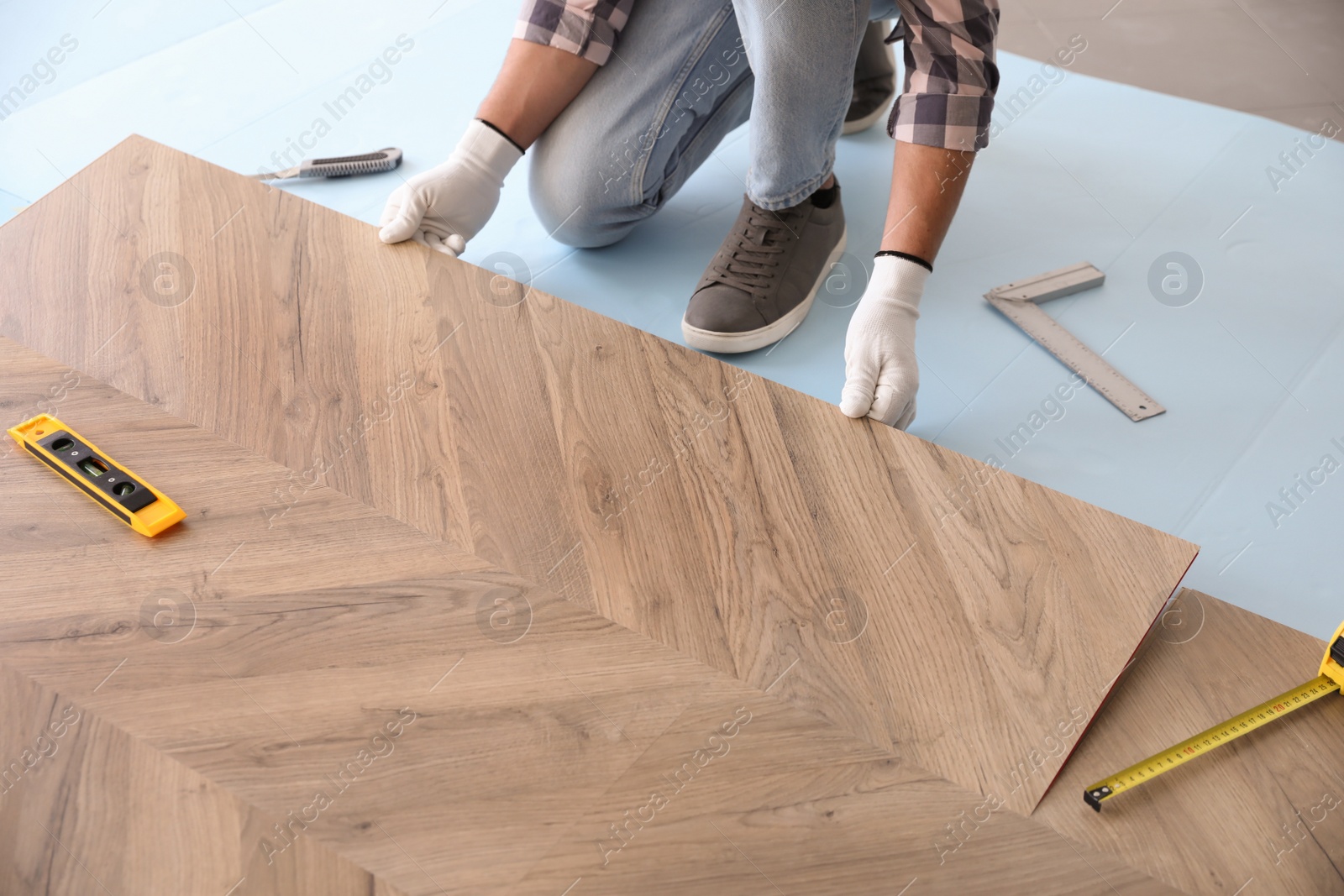 Photo of Worker installing laminated wooden floor indoors, closeup