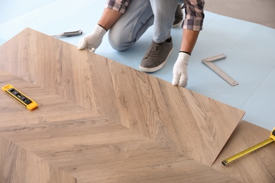 Photo of Worker installing laminated wooden floor indoors, closeup