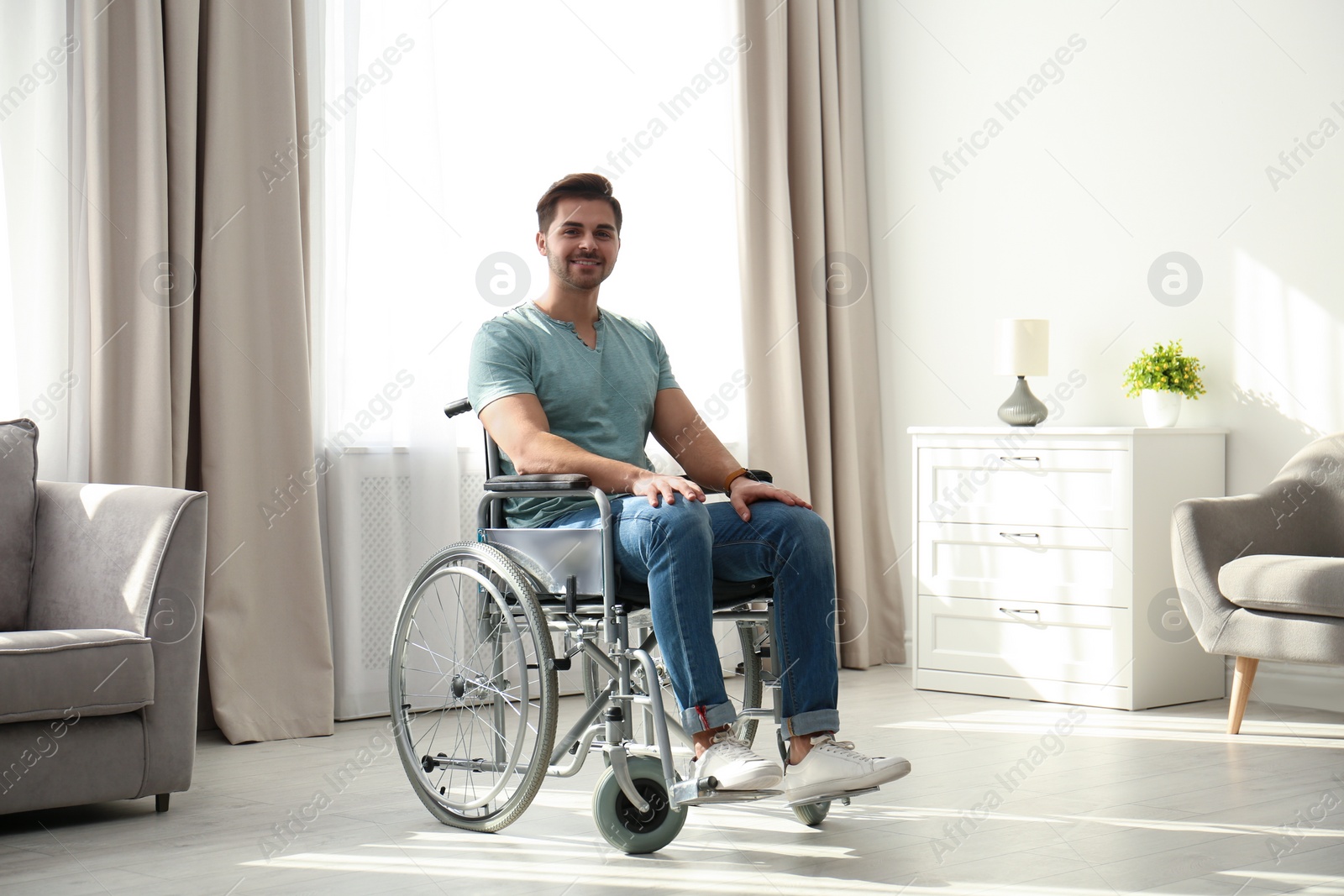 Photo of Young man sitting in modern wheelchair indoors