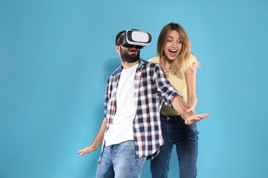 Photo of Young man playing video games with VR headset and emotional woman on color background