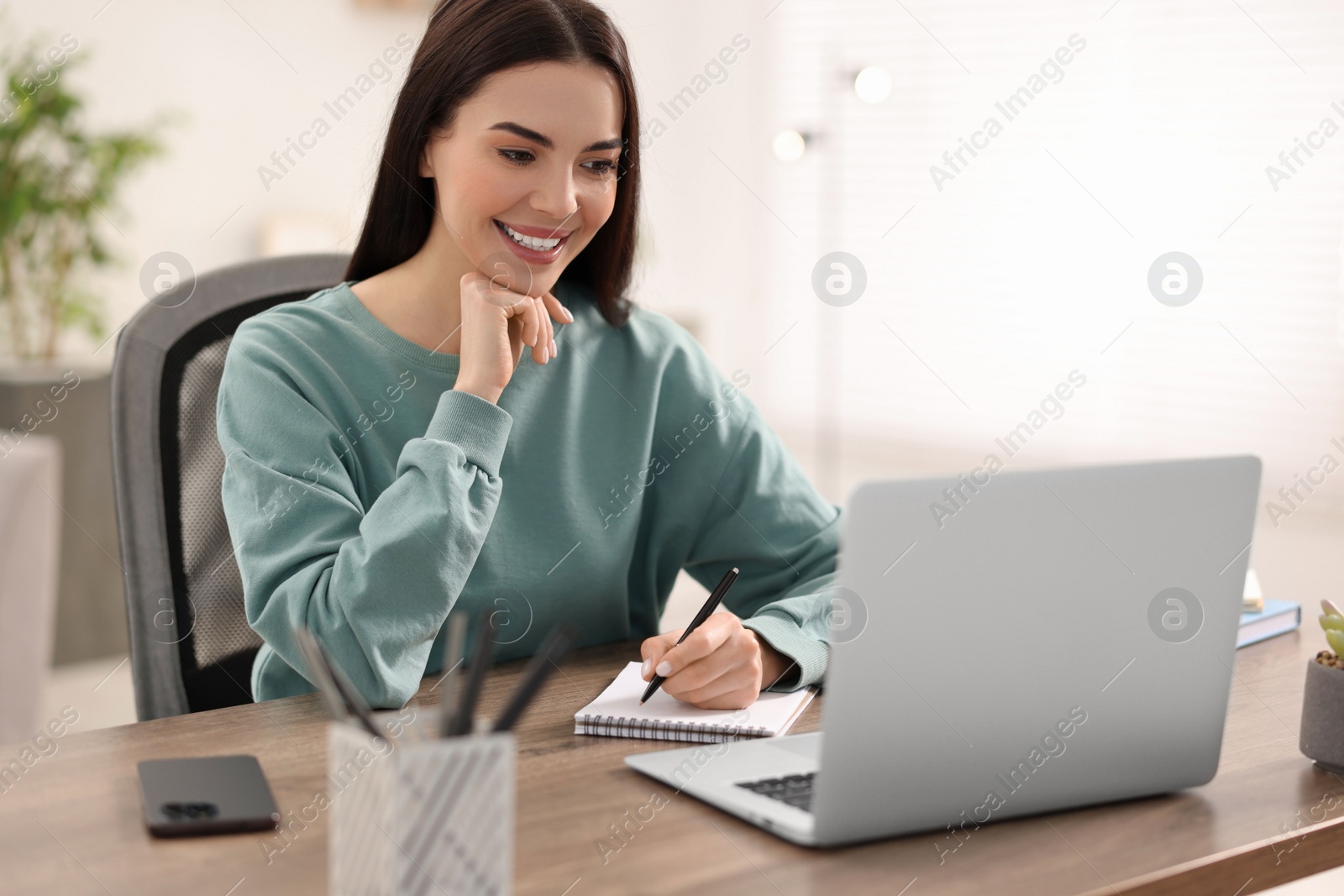 Photo of Young woman watching webinar at table in room