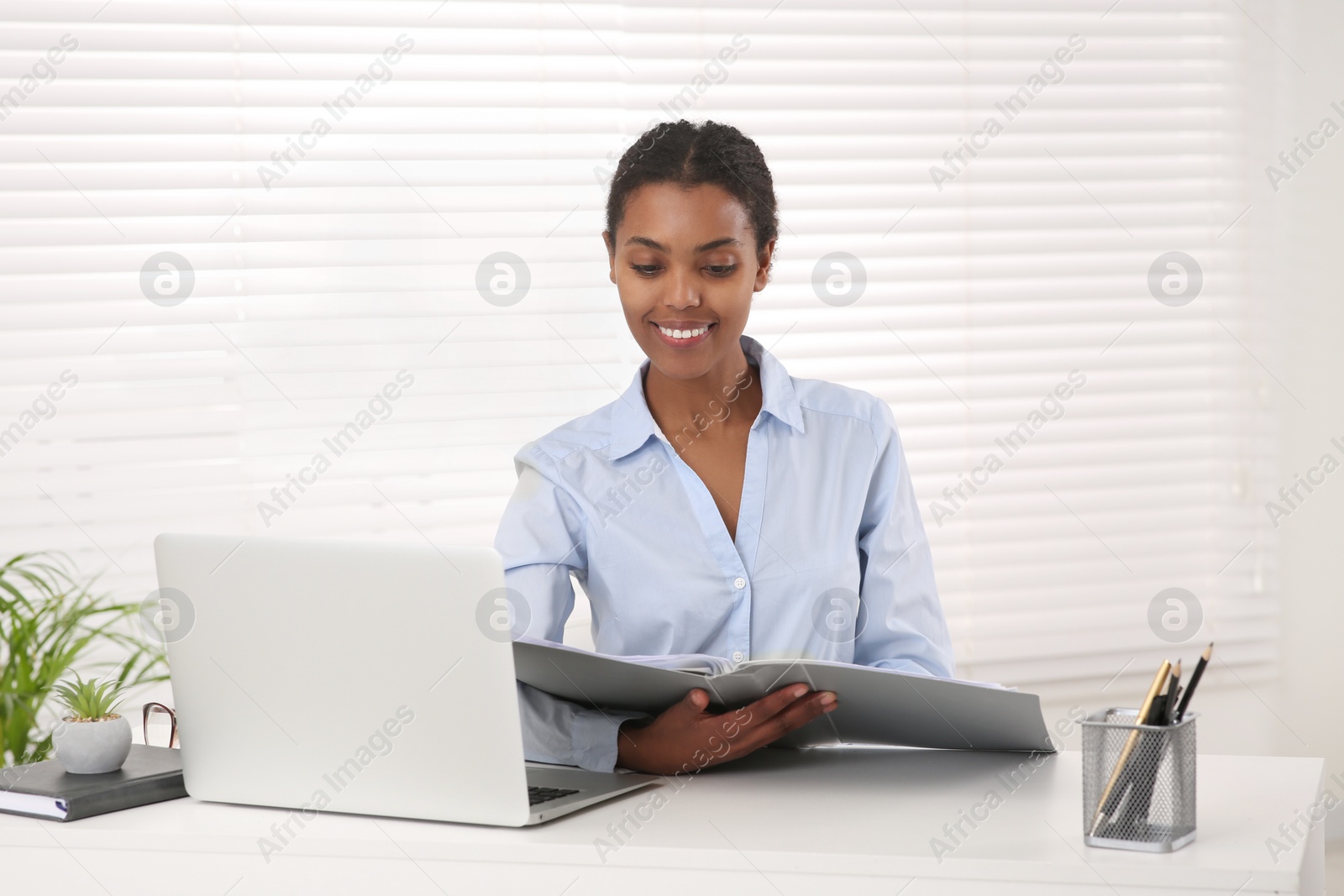 Photo of African American intern with folder working at white table in office