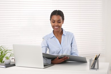 Photo of African American intern with folder working at white table in office