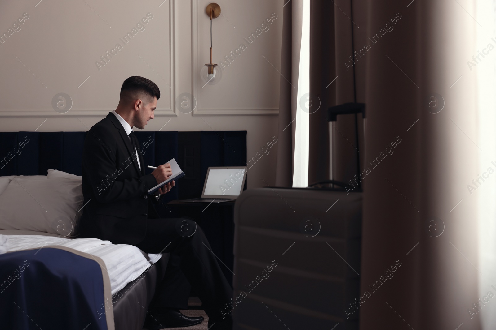 Photo of Handsome businessman working on bed in hotel room