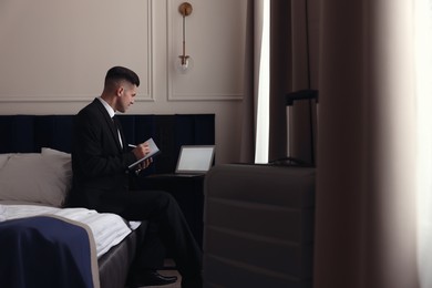 Photo of Handsome businessman working on bed in hotel room