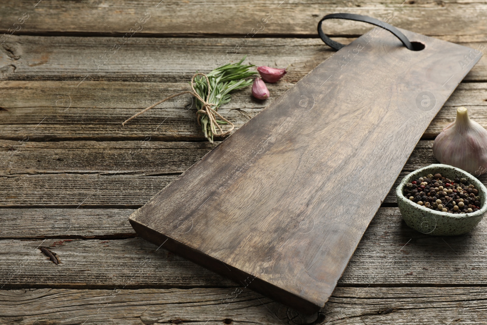 Photo of Cutting board, garlic, pepper and rosemary on wooden table. Space for text