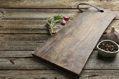 Photo of Cutting board, garlic, pepper and rosemary on wooden table. Space for text