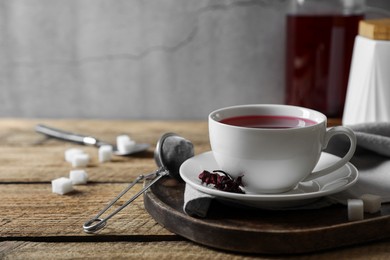 Delicious hibiscus tea in cup, strainer and sugar cubes on wooden table. Space for text