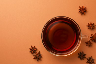 Cup of tea and anise stars on brown background, flat lay. Space for text