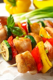 Photo of Delicious chicken shish kebabs with vegetables on parchment, closeup