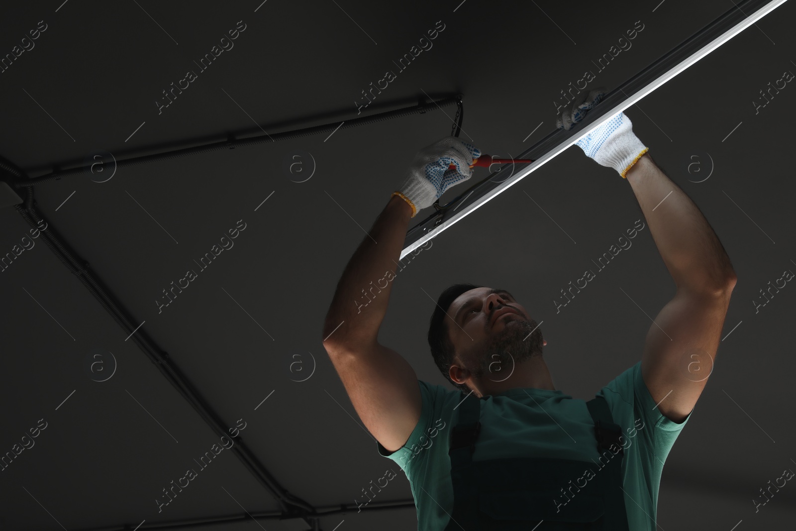 Photo of Ceiling light. Electrician installing led linear lamp indoors, low angle view. Space for text