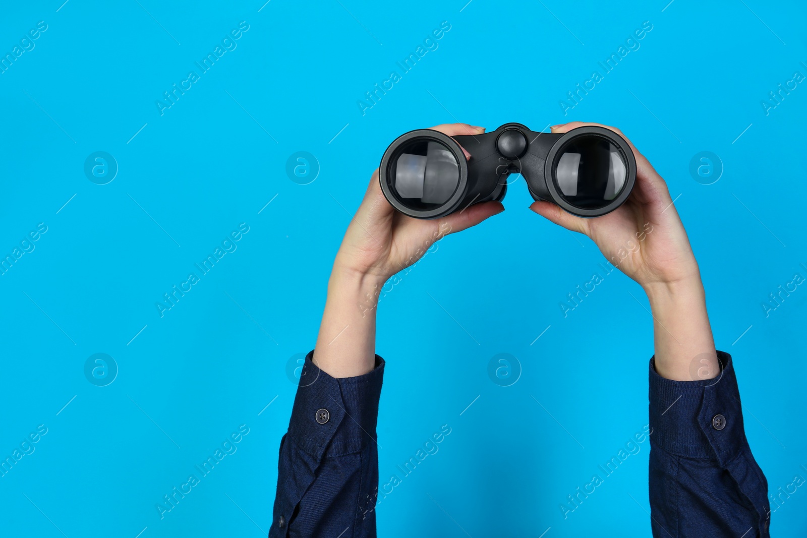 Photo of Woman holding modern binoculars on light blue background, closeup. Space for text