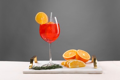 Photo of Glass of tasty Aperol spritz cocktail with orange slices and rosemary on white table against gray background