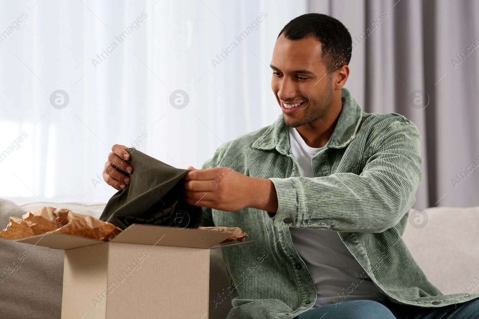 Photo of Happy young man opening parcel at home. Internet shopping