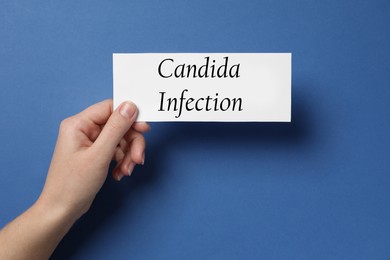 Woman holding white card with phrase Candida Infection on blue background, top view