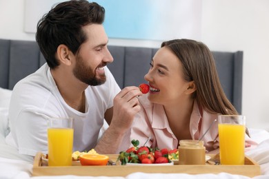 Photo of Tasty breakfast. Happy husband feeding his wife on bed at home