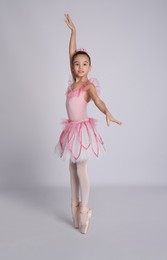 Photo of Beautifully dressed little ballerina dancing on grey background