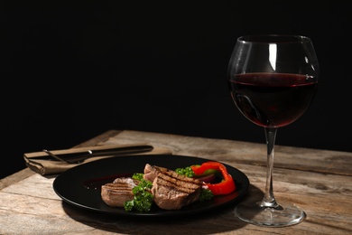 Photo of Grilled meat served with garnish and wine on table against black background. Space for text