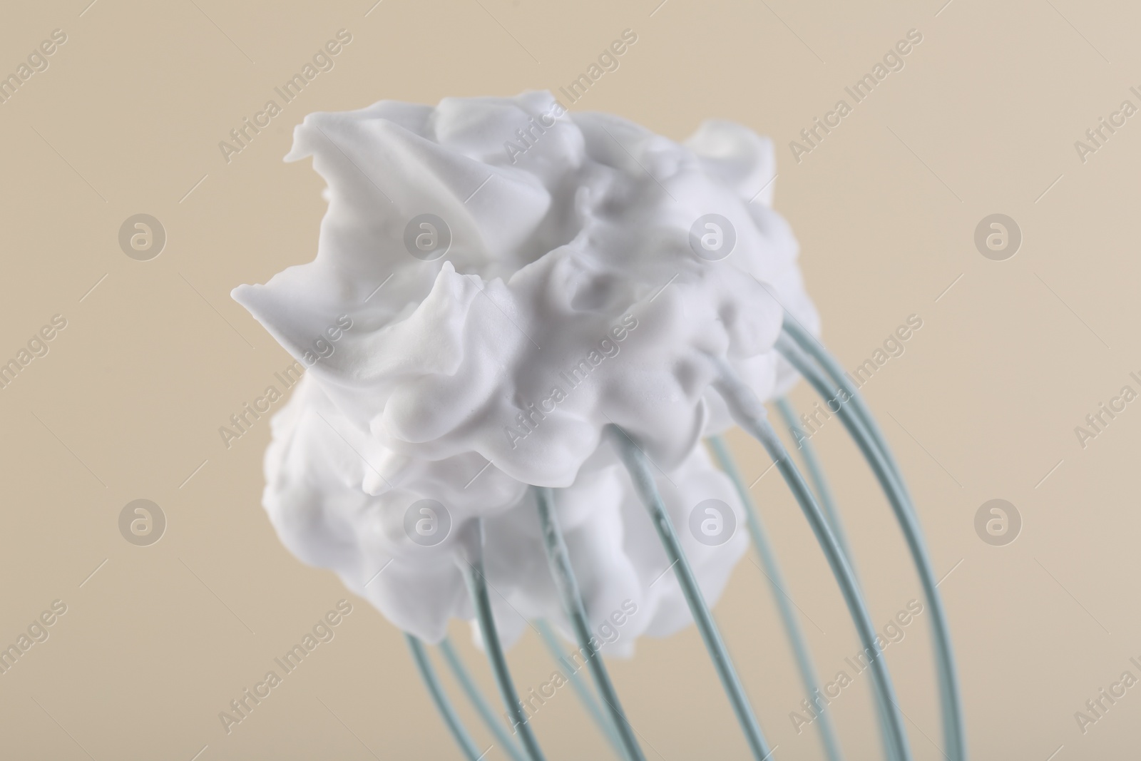 Photo of Whisk with whipped cream on beige background, closeup