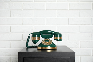 Photo of Green vintage corded phone on small black table near white brick wall