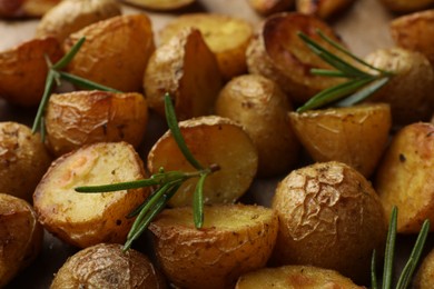 Photo of Tasty baked potato and aromatic rosemary on parchment paper, closeup