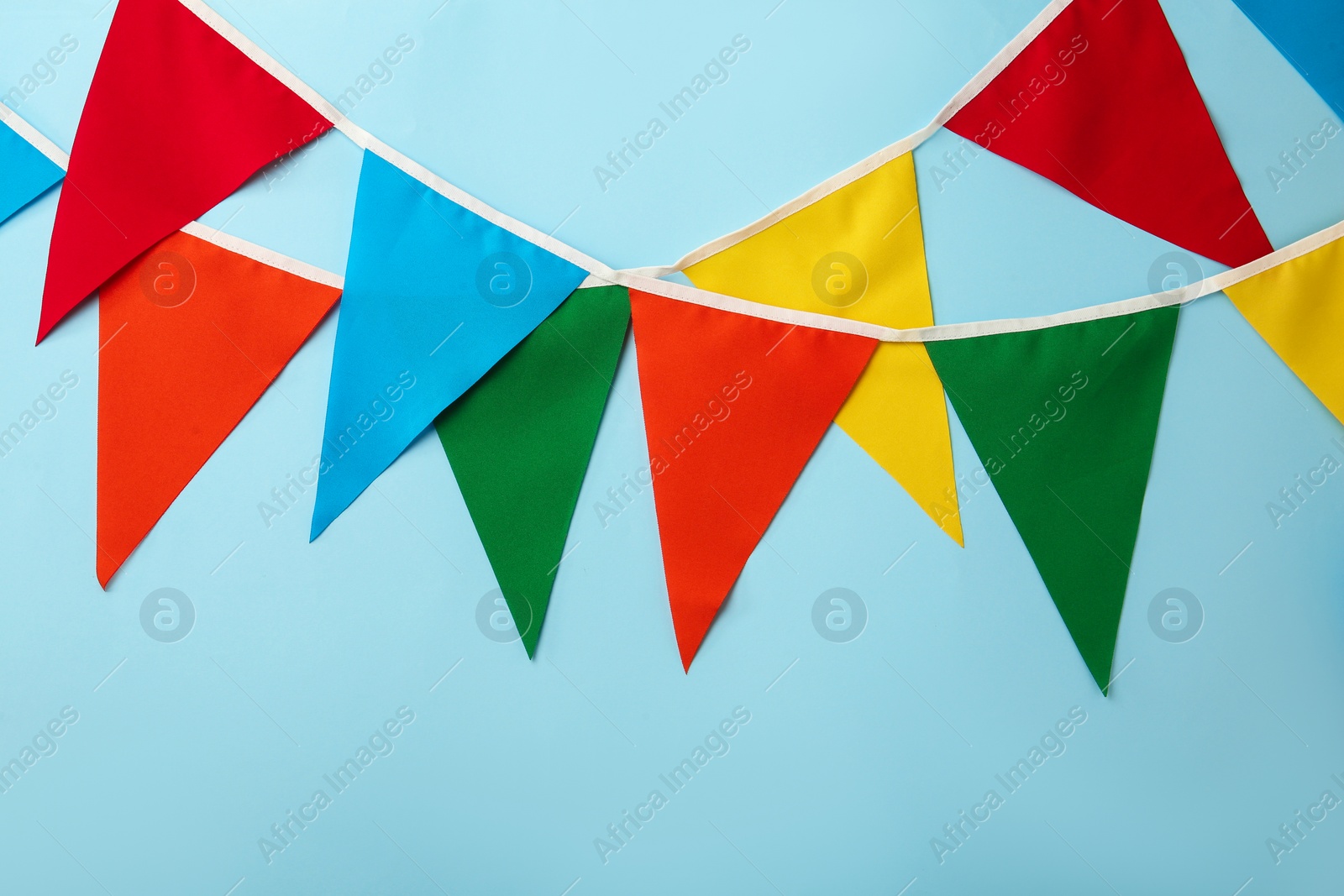 Photo of Buntings with colorful triangular flags on light blue background. Festive decor