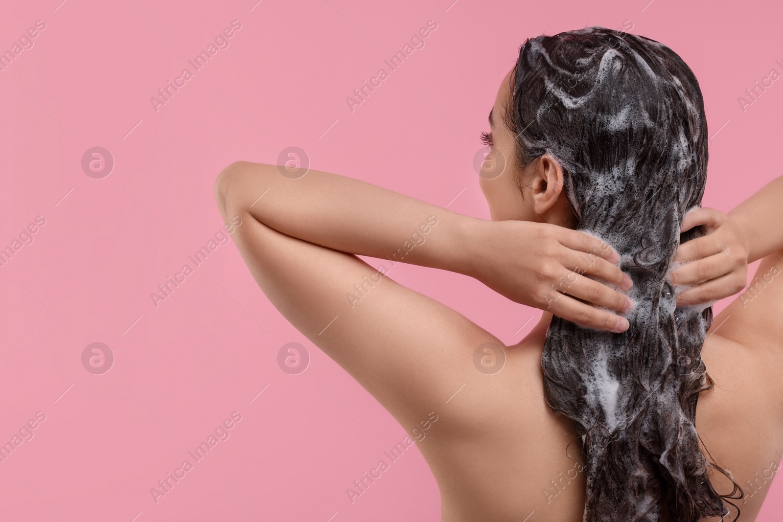 Photo of Woman washing hair on pink background, back view. Space for text